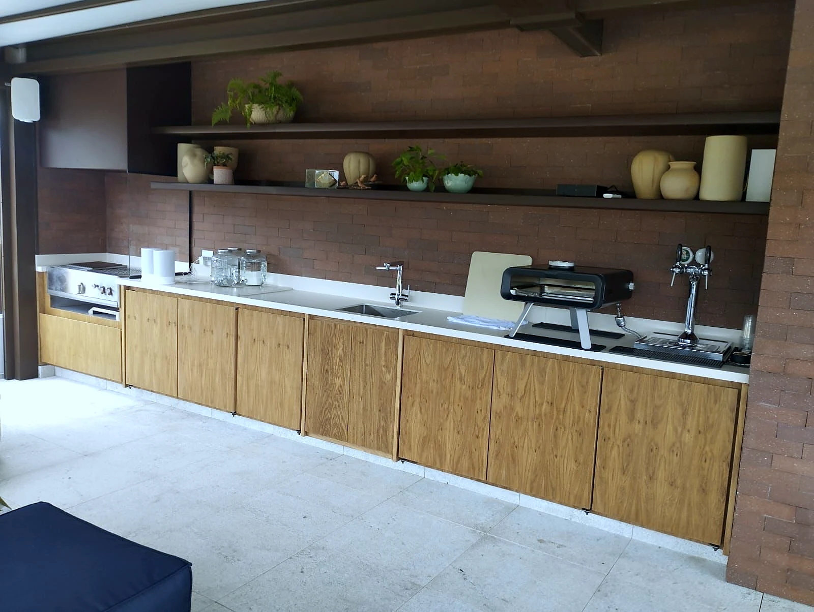 Área gourmet com bancada corrida em madeira, cuba em inox, cooktop e chopeira embutida no tampo