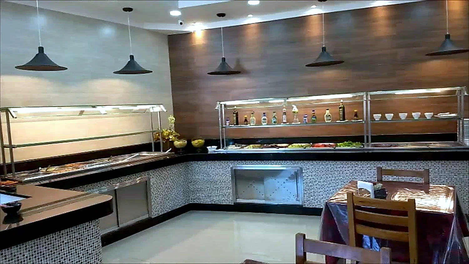 Salão de restaurante self-service com buffet em L, painel de madeira ao fundo e mesas postas